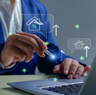 Imagem de uma pessoa usando um laptop com gráficos e ícones de casa, porcentagem e aumento, simbolizando análises imobiliárias e mercado de imóveis.
