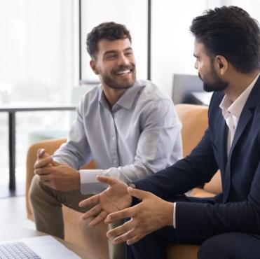 Homem de negócios sorridente conversando com colega durante reunião informal no escritório moderno, transmitindo confiança e parceria.