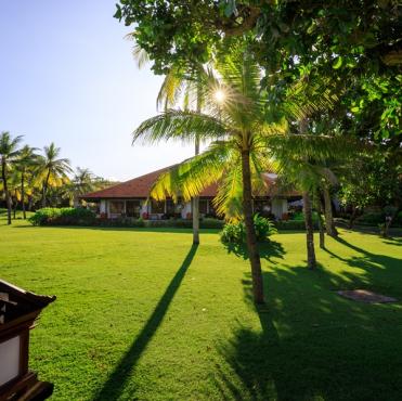 Entardecer em uma pousada tropical com gramado bem cuidado, palmeiras e árvores, criando um cenário paradisíaco e relaxante na praia.