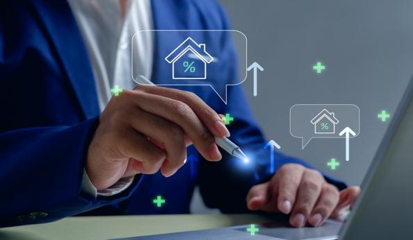 Imagem de uma pessoa usando um laptop com gráficos e ícones de casa, porcentagem e aumento, simbolizando análises imobiliárias e mercado de imóveis.