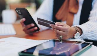  Uma pessoa segura um cartão de crédito e um smartphone, realizando uma transação digital ou pagamento online.