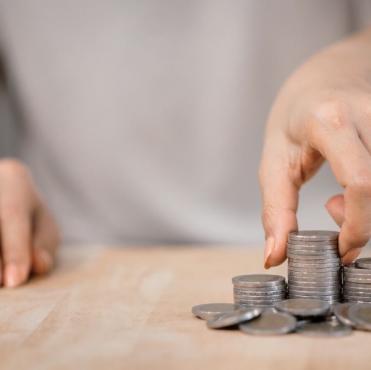Pessoa organizando moedas de diferentes tamanhos em uma superfície de madeira, simbolizando economia, finanças ou gestão financeira.