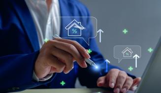 Imagem de uma pessoa usando um laptop com gráficos e ícones de casa, porcentagem e aumento, simbolizando análises imobiliárias e mercado de imóveis.