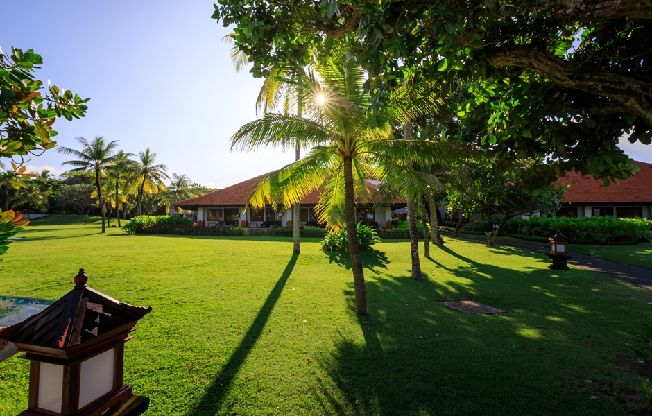 Entardecer em uma pousada tropical com gramado bem cuidado, palmeiras e árvores, criando um cenário paradisíaco e relaxante na praia.