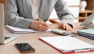  Uma pessoa em traje social organiza suas finanças utilizando uma calculadora e fazendo anotações em um caderno.