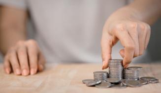 Pessoa organizando moedas de diferentes tamanhos em uma superfície de madeira, simbolizando economia, finanças ou gestão financeira.