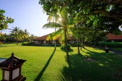 Entardecer em uma pousada tropical com gramado bem cuidado, palmeiras e árvores, criando um cenário paradisíaco e relaxante na praia.