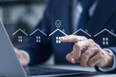 Pessoa de terno interagindo com uma tela digital que mostra ícones de casas e uma marca de verificação, simbolizando aprovação ou compra de imóveis, em um ambiente de escritório.