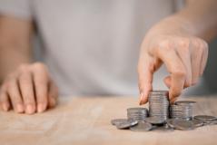 Pessoa organizando moedas de diferentes tamanhos em uma superfície de madeira, simbolizando economia, finanças ou gestão financeira.