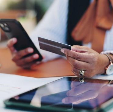  Uma pessoa segura um cartão de crédito e um smartphone, realizando uma transação digital ou pagamento online.