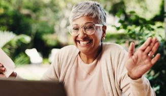 Mulher idosa sorrindo e acenando durante uma videochamada, transmitindo alegria e conexão emocional ao usar a tecnologia para manter contato com entes queridos.