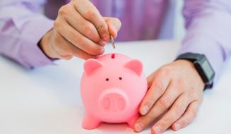 Mão depositando uma moeda em um cofrinho rosa, simbolizando o hábito de poupar e a importância do planejamento financeiro para o futuro.