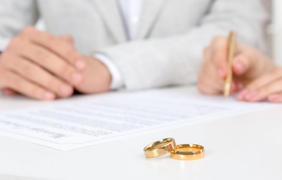 Casal assinando contrato de casamento com alianças de ouro em destaque na mesa, simbolizando união e compromisso matrimonial.