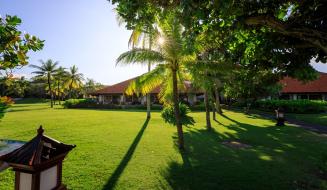 Entardecer em uma pousada tropical com gramado bem cuidado, palmeiras e árvores, criando um cenário paradisíaco e relaxante na praia.
