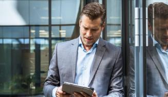 Homem de negócios usando tablet ao lado de vidro com reflexo, em ambiente corporativo moderno