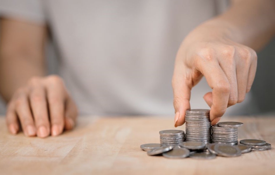 Pessoa organizando moedas de diferentes tamanhos em uma superfície de madeira, simbolizando economia, finanças ou gestão financeira.