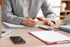  Uma pessoa em traje social organiza suas finanças utilizando uma calculadora e fazendo anotações em um caderno.