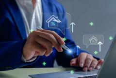 Imagem de uma pessoa usando um laptop com gráficos e ícones de casa, porcentagem e aumento, simbolizando análises imobiliárias e mercado de imóveis.